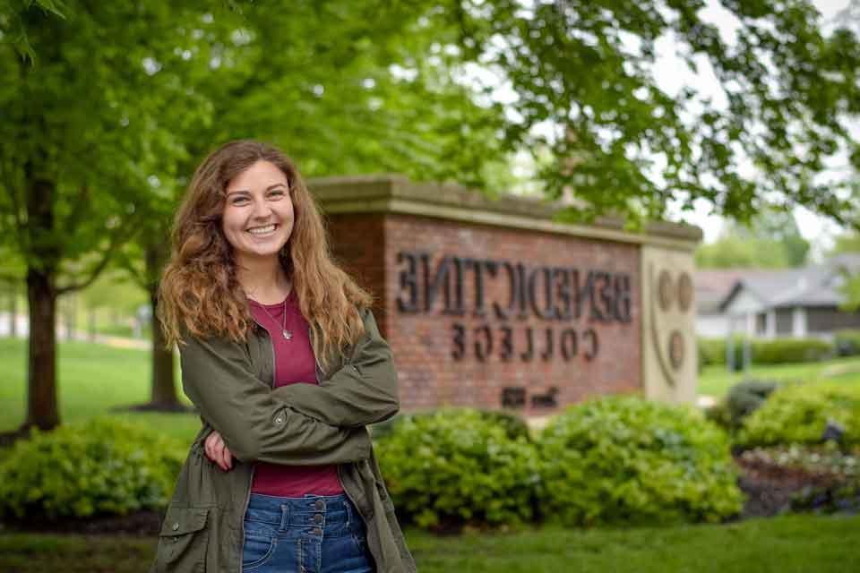 A student poses for a photo near the Benedictine College entrance sign
